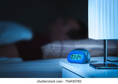 Man Sleeping In Bed. Digital Alarm Clock On Nightstand In Bedroom. Dreamy Blur Effect.