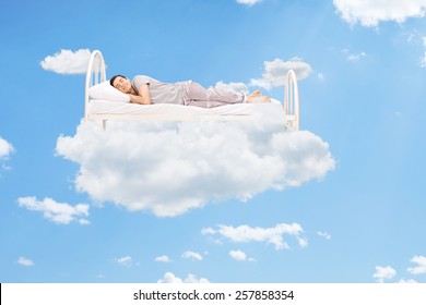 Man sleeping on a bed in the clouds high up in the sky