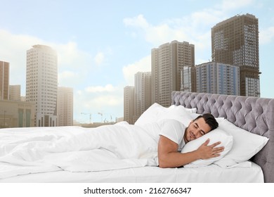 Man sleeping on bed with soft pillows and beautiful view of cityscape on background. Good sleep despite of urban bustle