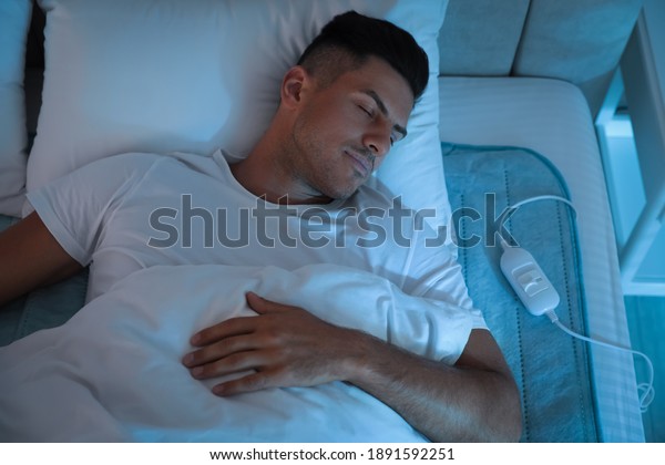 Man sleeping on electric heating pad in bed at\
night, above view