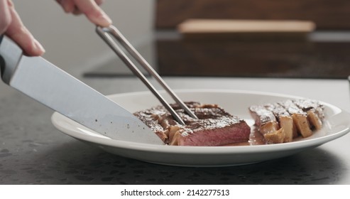 Man Slicing Ribeye Steak On A White Plate On Concrete Countertop