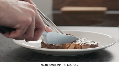 Man Slicing Ribeye Steak On A White Plate On Concrete Countertop