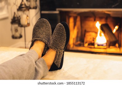 Man in slippers relaxing with his feet up - warm cozy cabin scene with a fireplace in the background. 