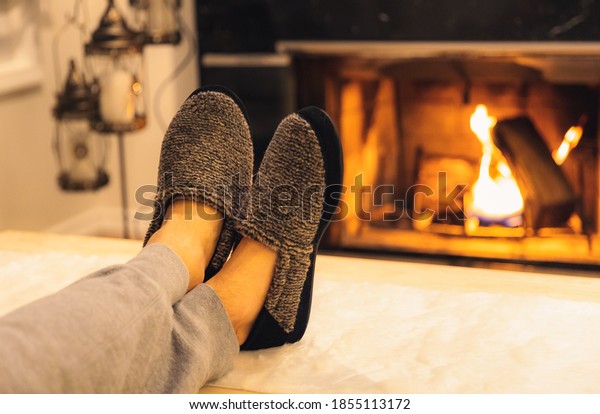 Man in slippers relaxing\
with his feet up - warm cozy cabin scene with a fireplace in the\
background. 