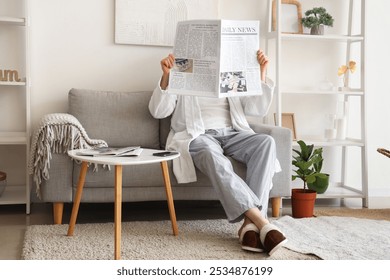 Man in slippers resting on sofa and reading newspaper at home - Powered by Shutterstock