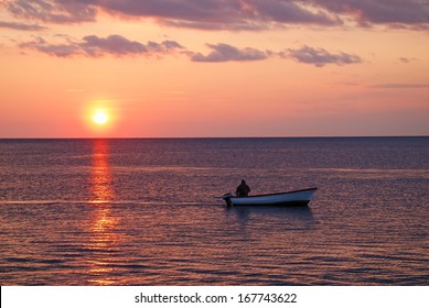 Man With Small Motor Boat In The Sea At Sunset