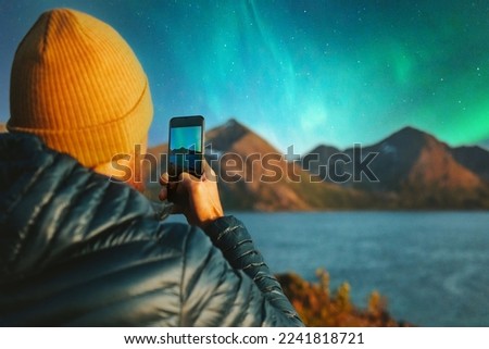 Man with smartphone taking photo of northern lights winter travel in Norway adventure vacations outdoor blogger influencer lifestyle modern online technology