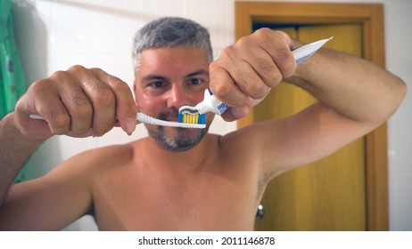 A Man Smears Toothpaste On A Toothbrush. Bathroom. Beard On The Face. Short Haircut. Tanned Skin. Close-up. Healthy Teeth. Dentistry. Toothpaste.