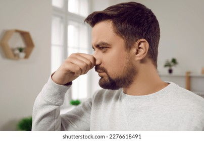 Man smells something bad at home. Young man pinches his nose as he feels a bad, unpleasant smell of something stinking in the house. Close up shot