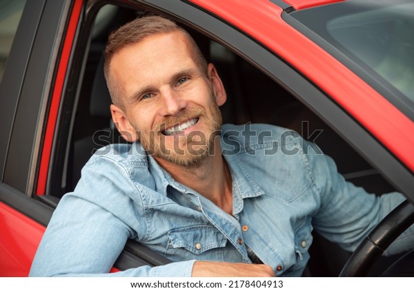 A man with
a smile on his face drives a red
car.