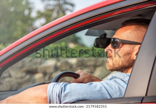 A man with\
a smile on his face drives a red\
car.