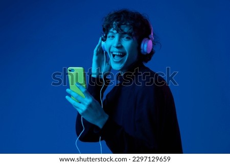 Man smile with phone in hand taking selfies with headphones listening to music, portrait dark blue background, neon light, style and trends, mixed light, men's fashion, copy spot