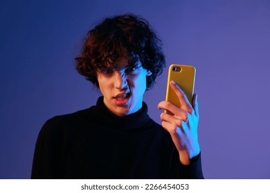 Man smile with phone in hand teenager talking via smartphone online, video call and selfies, hipster lifestyle, portrait purple background, mixed neon light, fashion style and trends, copy space - Powered by Shutterstock