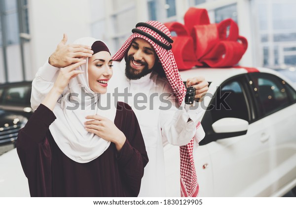 A man smiles and gives a woman keys to a new car at
a car dealership. A woman looks at the keys that a man holds for
her as a gift.