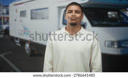 Man smiles showing teeth while standing by a camper van on street wearing a cream polo and goatee; joyful road trip.