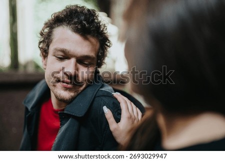 A man smiles warmly while a supportive hand rests on his shoulder, expressing care and encouragement. The close-up captures emotions of compassion, understanding, and connection in an outdoor setting.
