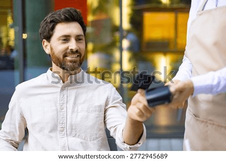 A man smiles while holding out a credit card to a server holding a payment terminal for a transaction