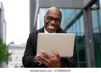 Man smiles while using laptop outdoors in urban setting during daytime