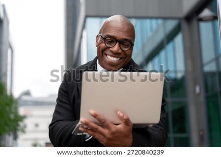Man smiles while using laptop outdoors in urban setting during daytime