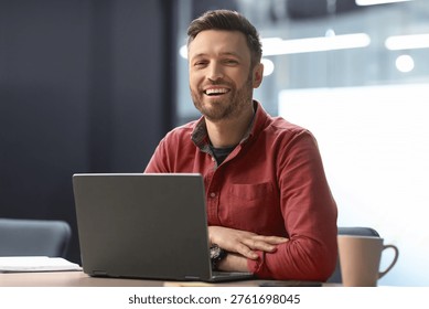 Man Smiles While Working on Laptop in Office Setting During Daytime Hours