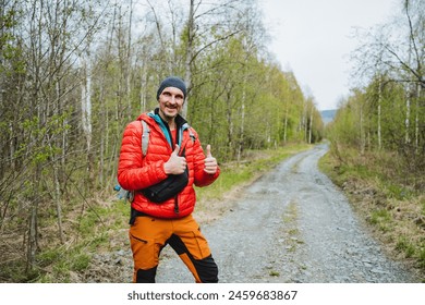 A man smiling with a backpack on a dirt road surrounded by a natural landscape of trees, grass, and a clear sky, symbolizing travel and recreation in the serene landscape - Powered by Shutterstock