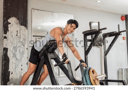 A man smiling confidently before doing a set of plate loaded chest-supported rows. back workout at the gym.