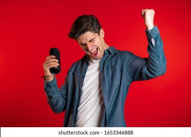 Man Smiling, Dancing With Wireless Portable Speaker In Studio On Red Background. Music, Dance Concept.