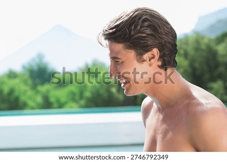 Man smiling and facing left, posing shirtless at pool edge with pool water, copy space. Barechest, male, outdoor, sunlit, turquoise, deck, trees