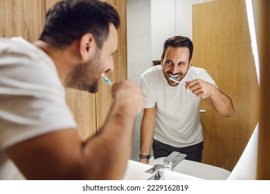 A man is smiling at the mirror and brushing his teeth at the bathroom. - Powered by Shutterstock