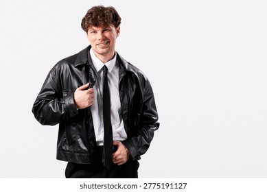 Man smiling and posing in a studio, wearing a fashionable black leather jacket, white shirt, and black tie