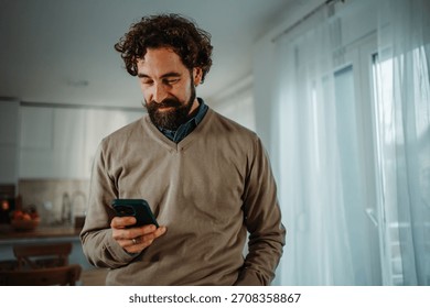 Man smiling while checking phone, enjoying digital connection at home
