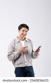 A man is smiling while holding a cell phone. He is wearing a grey jacket and blue jeans