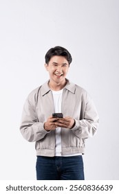 A man is smiling while holding a cell phone. He is wearing a grey jacket and blue jeans