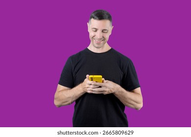 A man is smiling while holding a cell phone. The phone is yellow and the man is wearing a black shirt