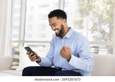 Man smiling while look at smartphone screen, clenching fist in celebratory gesture, received positive news, approval of project, financial gain, opportunity, relish personal achievement or lottery win
