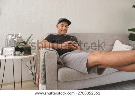 Man smiling while lounging on sofa, browsing social media on his mobile phone