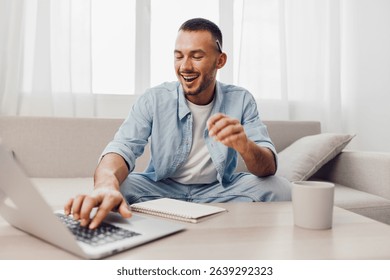 A man smiling while working on his laptop, reflecting themes of soft masculinity and the blend of work-life balance in a modern home.