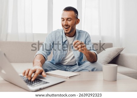 A man smiling while working on his laptop, reflecting themes of soft masculinity and the blend of work-life balance in a modern home.