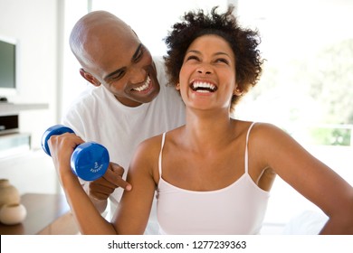 Man smiling at woman exercising with weights at home