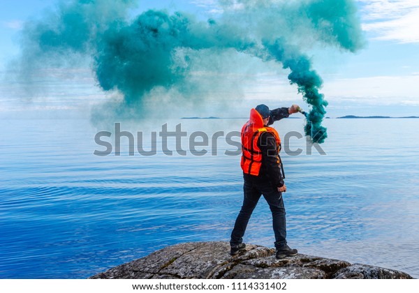 A man with a smoke torch. The rescue. Distress\
call. The man lights a smoke signal. A man in a life jacket. SOS.\
signal by smoke.