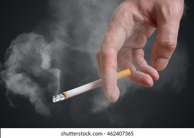 Man (smoker) Is Holding Cigarette In Hand On Black Background. Smoke Around.