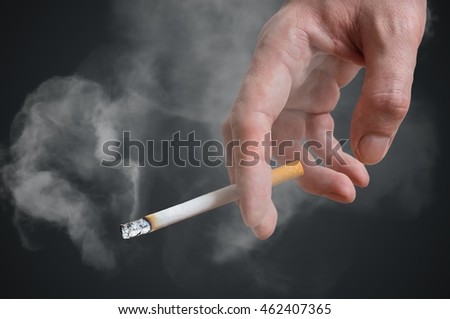 Man (smoker) is holding cigarette in hand on black background. Smoke around.