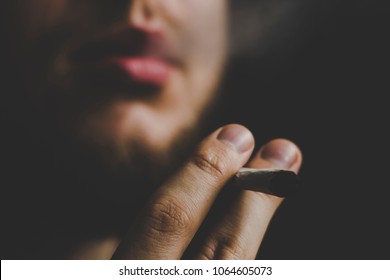 A Man Smokes Cannabis Weed, A Joint And A Lighter In His Hands. Smoke On A Black Background. Concepts Of Medical Marijuana Use And Legalization Of The Cannabis. On A Black Background