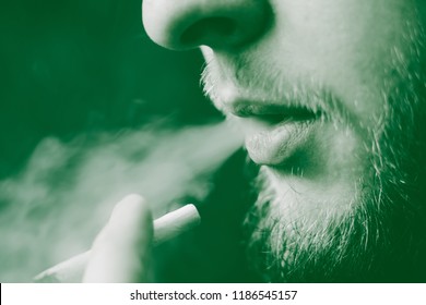 A Man Smokes Cannabis Weed, A Joint And A Lighter In His Hands. Smoke On A Black Background. Concepts Of Medical Marijuana Use And Legalization Of The Cannabis. On A Black Background