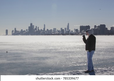 A man smokes a cigar and steam rises from Lake Michigan on a freezing cold day at the lakefront with the Chicago skyline in the background.
