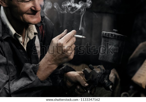 Man smokes in garage. Auto Mechanic.\
Professional car painter in\
garage.\
