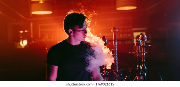 man smokes a hookah and lets out a cloud of smoke in the interior of the restaurant