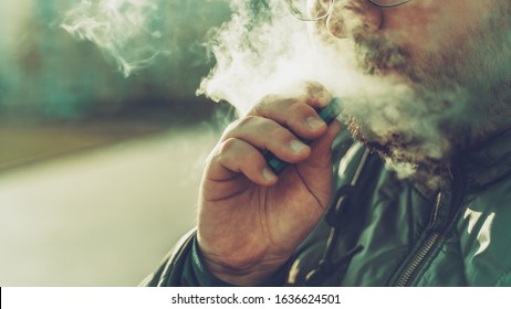 Man smokes new Vape Pod System, exhales vapor of electronic cigarette, vaping concept, selective focus, copy space.