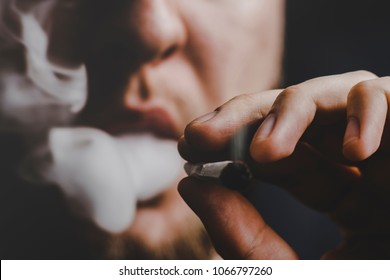 A man smokes weed cannabis a joint and a lighter in his hands. Smoke on a black background. Concepts of medical marijuana use and legalization of the cannabis. On a black background