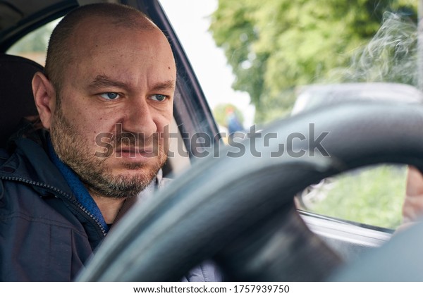 A man smokes at the\
wheel of a car.